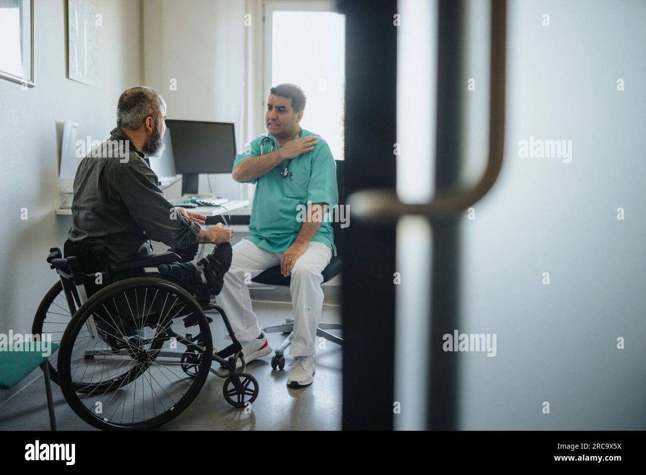 Arztbesprechung mit männlichem Patienten im Rollstuhl in der Klinik Stockfoto