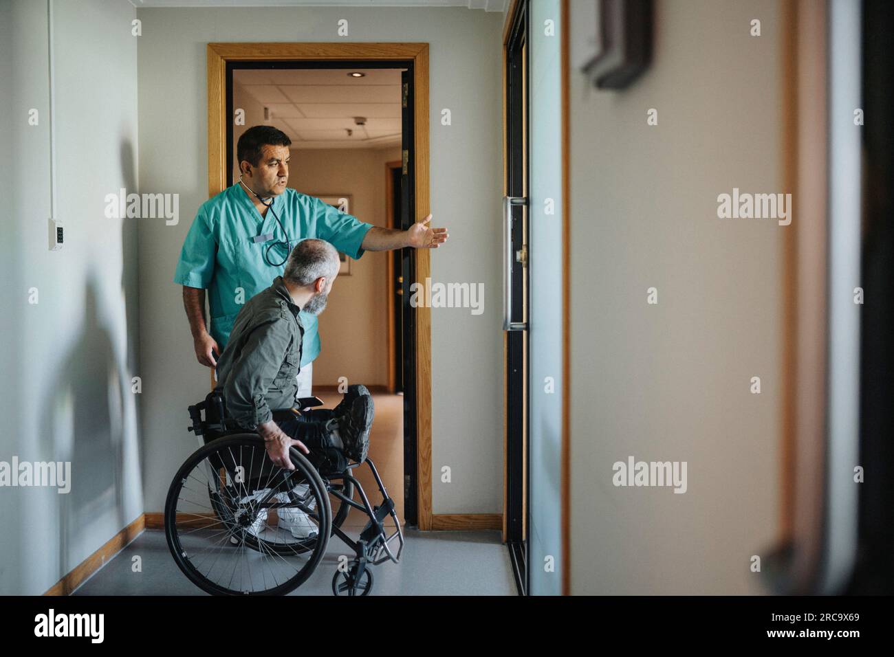 Arzt weist männlichen Patienten im Rollstuhl in Richtung Klinikeingang Stockfoto
