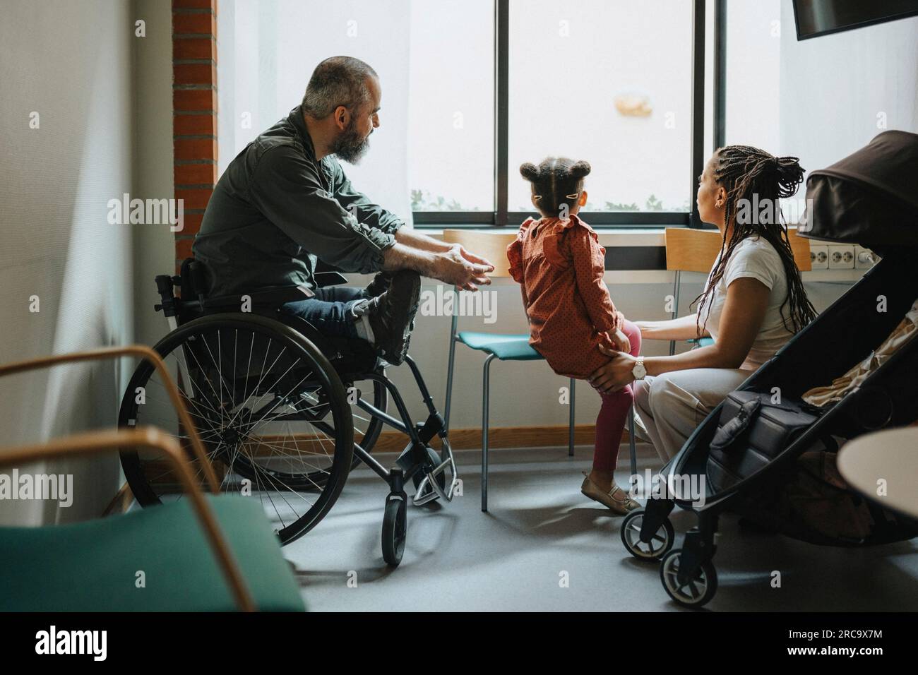 Mutter und Tochter, die im Rollstuhl im Krankenhaus durch das Fenster schauen Stockfoto