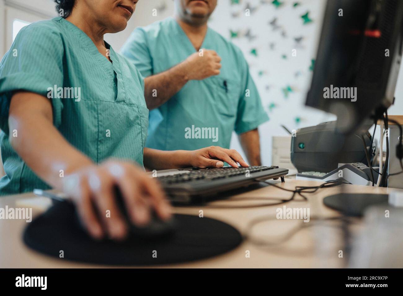 Mittelschicht einer Krankenschwester mit Computer durch einen Kollegen an der Rezeption im Krankenhaus Stockfoto