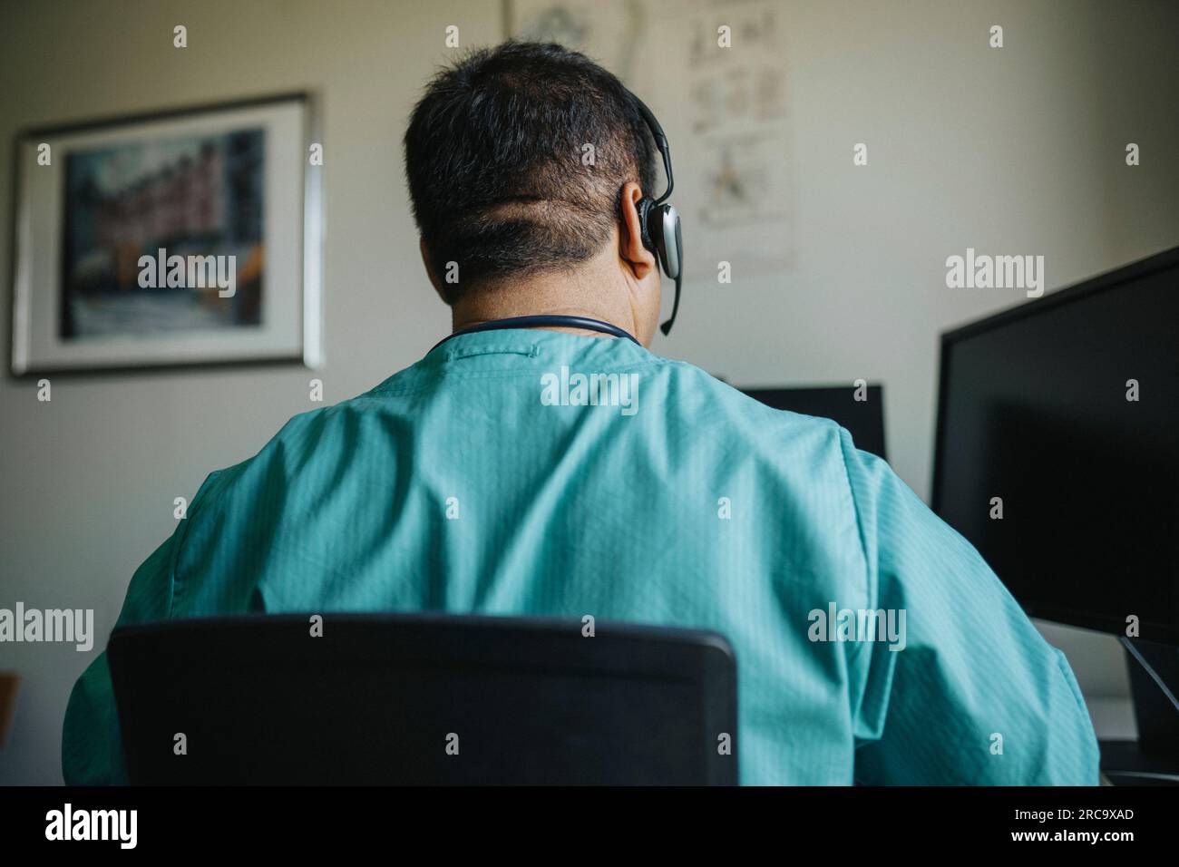 Rückansicht eines Arztes, der während der Online-Konsultation ein Headset am Computer trägt Stockfoto