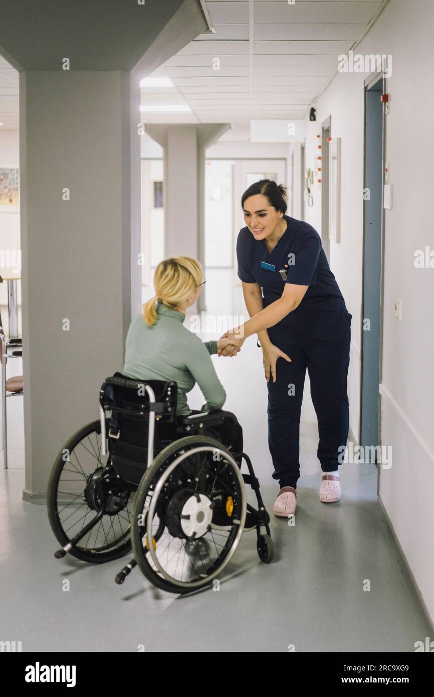 Lächelnde weibliche Krankenschwester grüßt Patientin im Rollstuhl im Krankenhaus Stockfoto