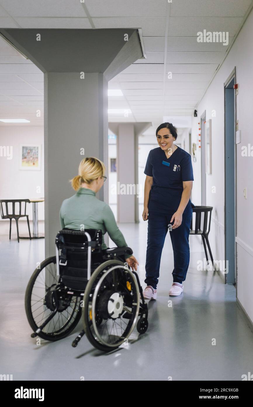Lächelnde weibliche Pflegekraft, die im Krankenhaus auf eine behinderte Patientin zugeht Stockfoto