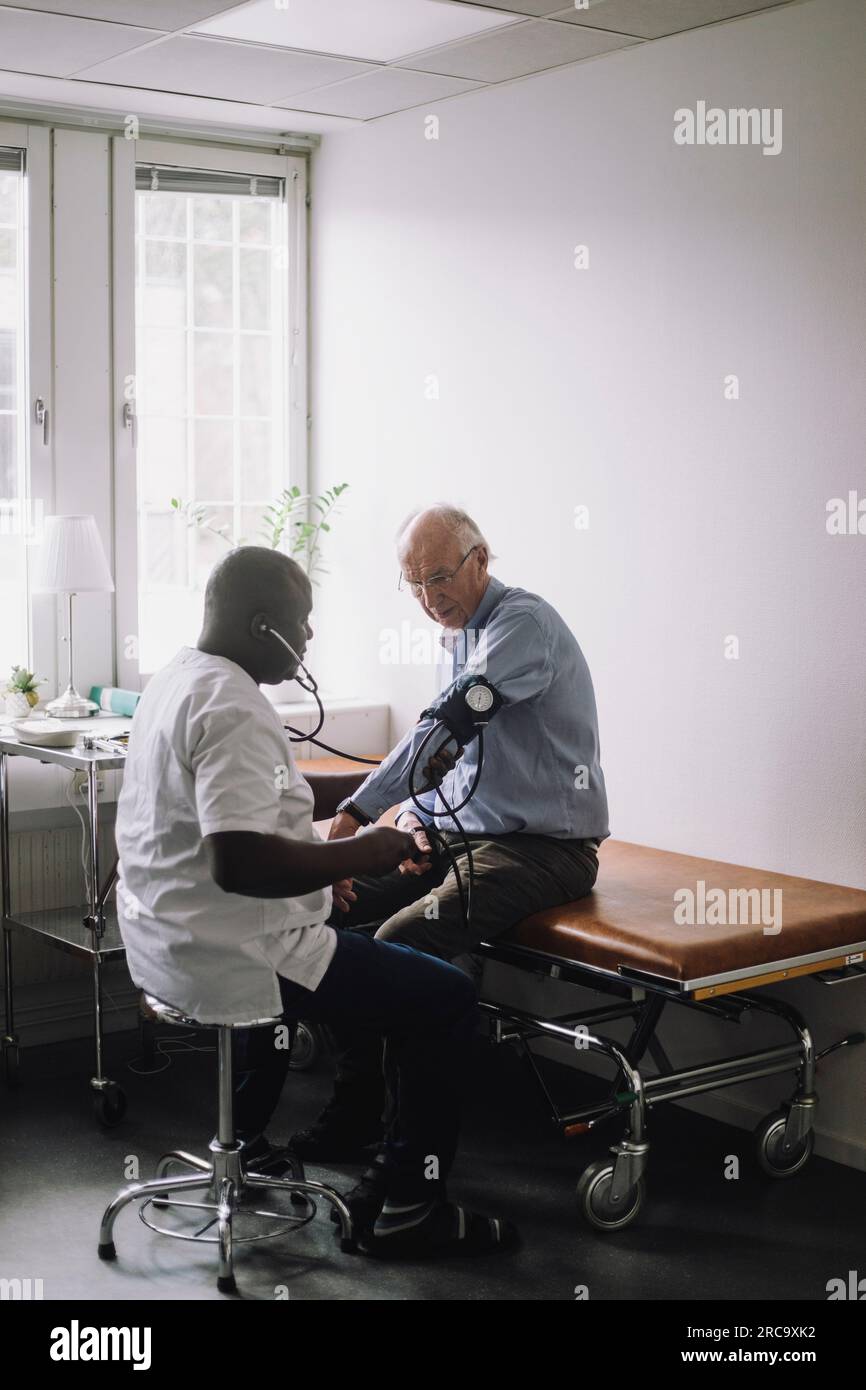 Reifungsarzt zur Blutdruckkontrolle des leitenden männlichen Patienten im Klinikaufenthalt Stockfoto