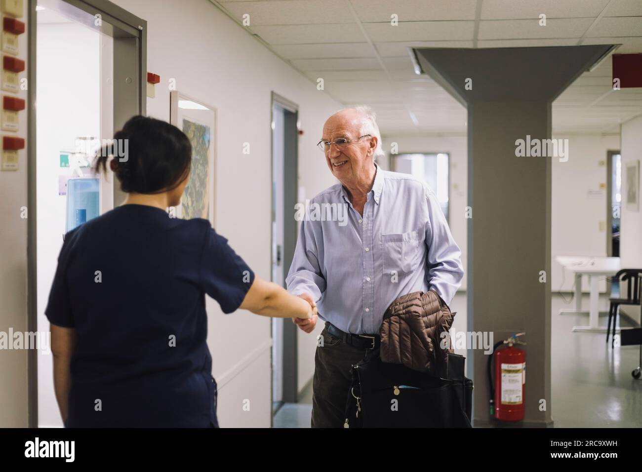 Lächelnder älterer Mann begrüßt weibliches medizinisches Personal, das im Krankenhaus steht Stockfoto