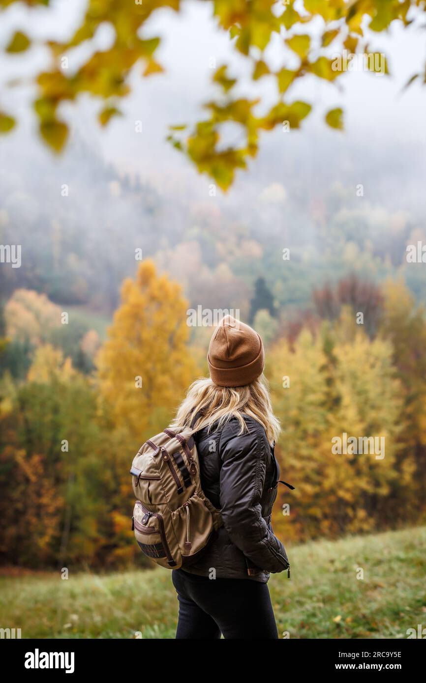 Wandern im Herbstwald für Alleinreisende. Eine Frau mit Rucksack und Strickmütze, die in den Bergen reitet. Outdoor-Sportaktivitäten in der Herbstsaison Stockfoto