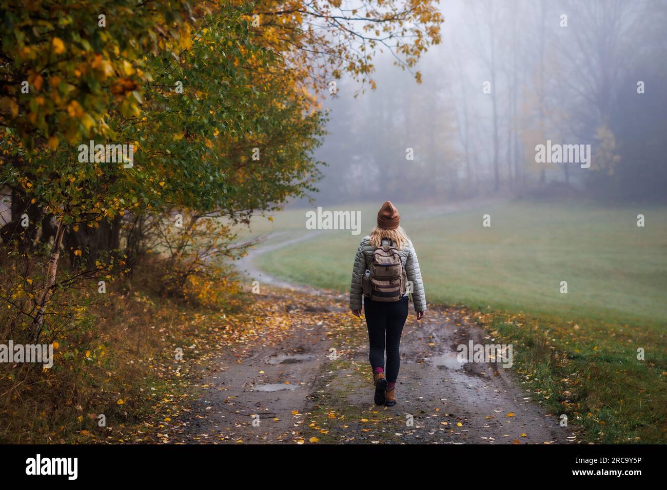 Frau auf Wanderwegen im Herbstwald. Nebelwetter. Alleinreisende auf unbefestigten Straßen auf dem Wanderweg Stockfoto