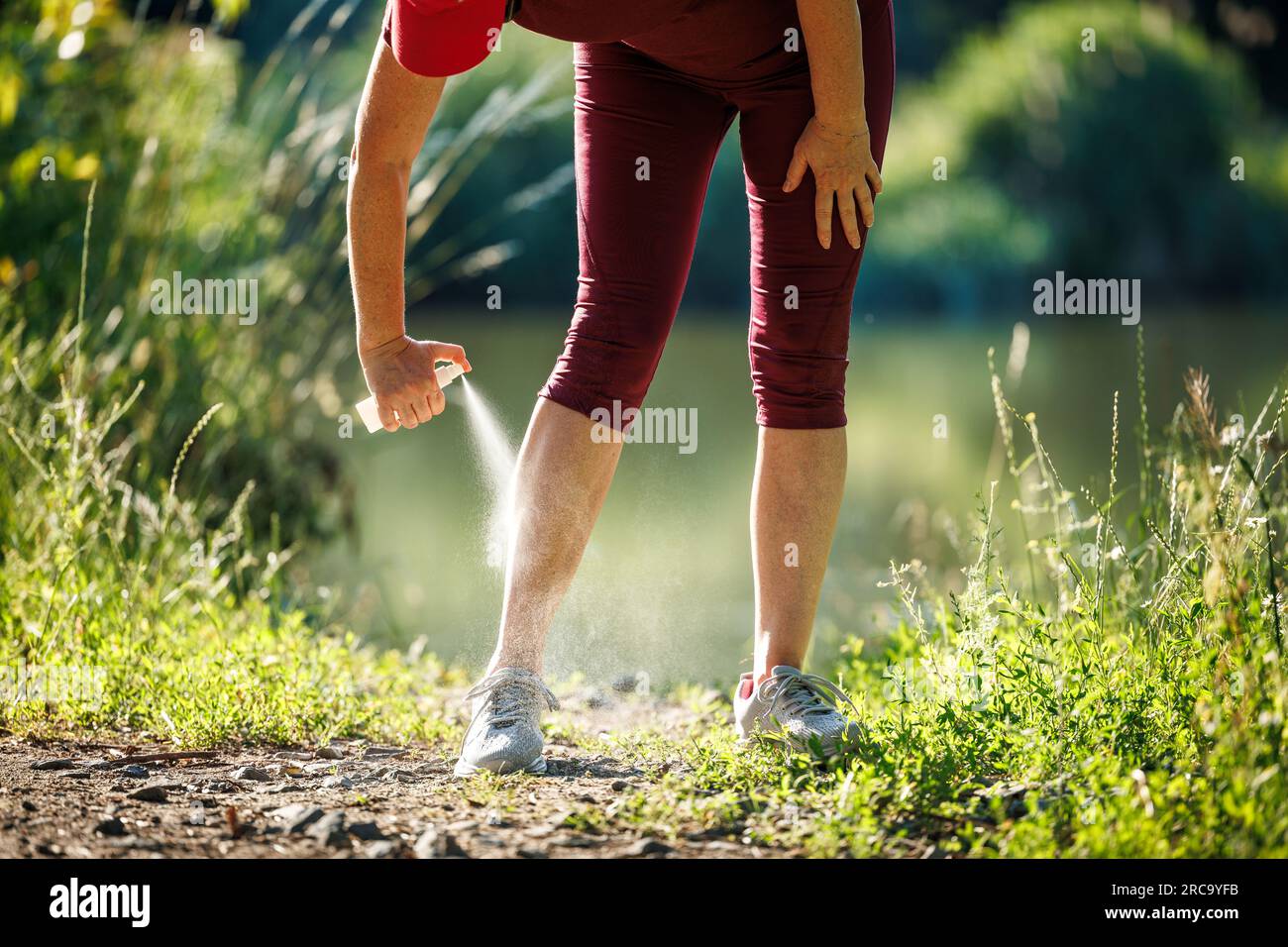 Frau, die Insektenschutzmittel gegen Mücken aufträgt und Zecken auf ihrem Bein aufträgt, bevor sie im Freien joggt Stockfoto