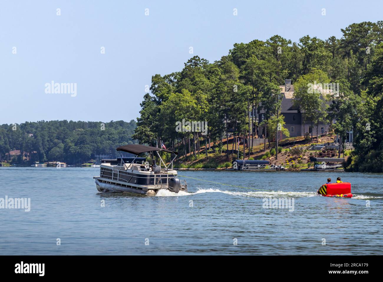 Ein Pontonboot, das aufblasbare Schlauchfloß auf dem See zieht. Familie auf einem Pontonpartyboot, die an einem Sommertag mit ihren Kindern Tubing genießt. Stockfoto