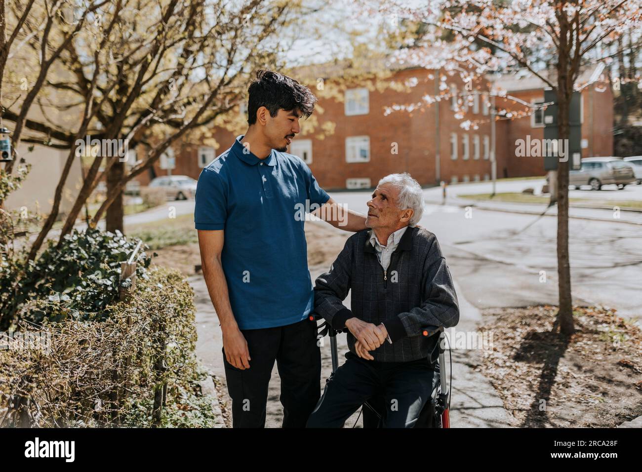 Pflegender Mann mit Hand auf Schulter eines älteren Mannes, der auf einem Geher sitzt Stockfoto
