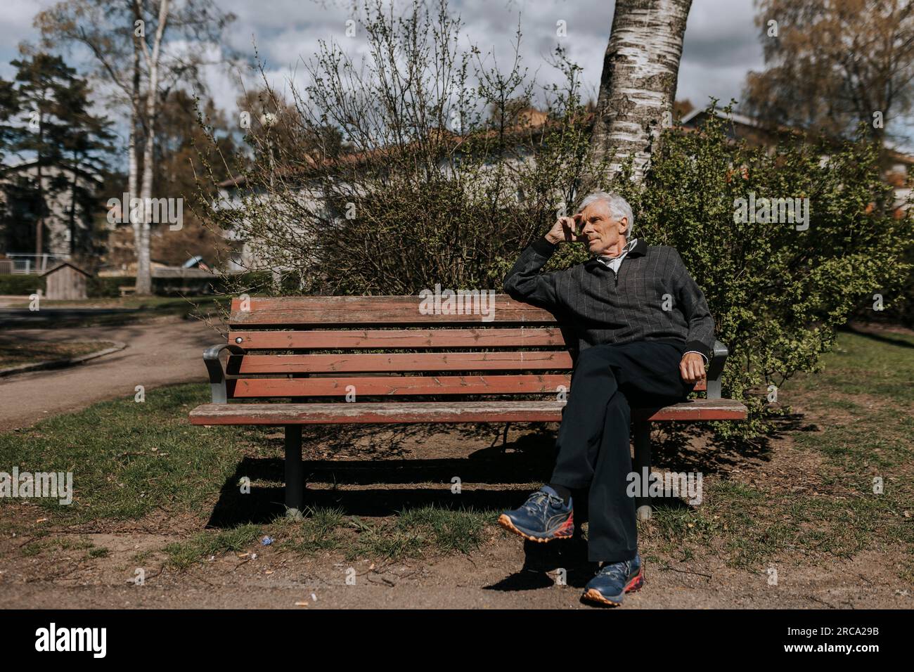 Seniorenmann, der an sonnigen Tagen auf einer Bank im Park sitzt Stockfoto