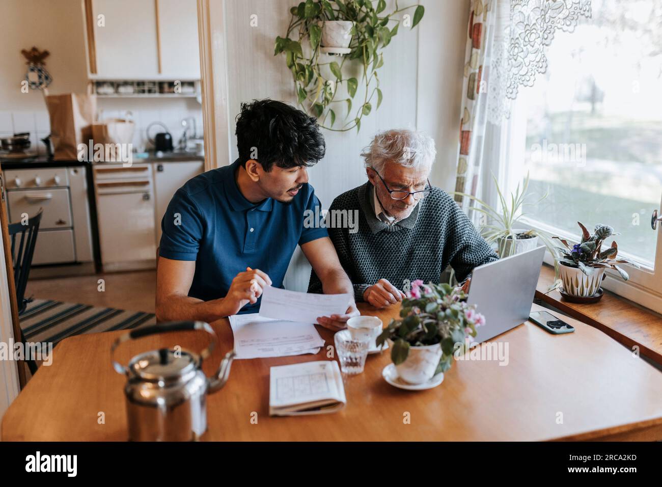 Pflegender Mann diskutiert medizinische Berichte mit Seniorenmann, der zu Hause ein Notebook benutzt Stockfoto