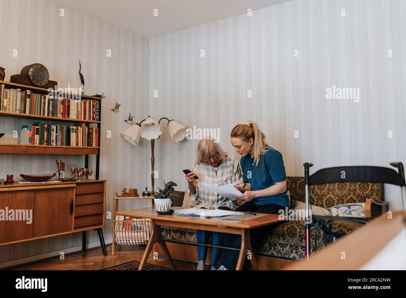 Pflegende Frau diskutiert mit Seniorin zu Hause über ärztliche Berichte Stockfoto