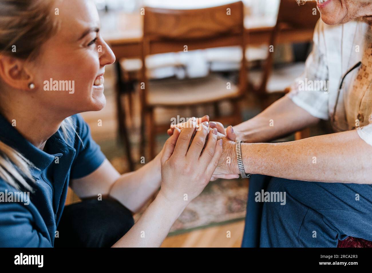 Lächelnde weibliche Pflegekraft, die zu Hause die Hände einer älteren Frau hält Stockfoto