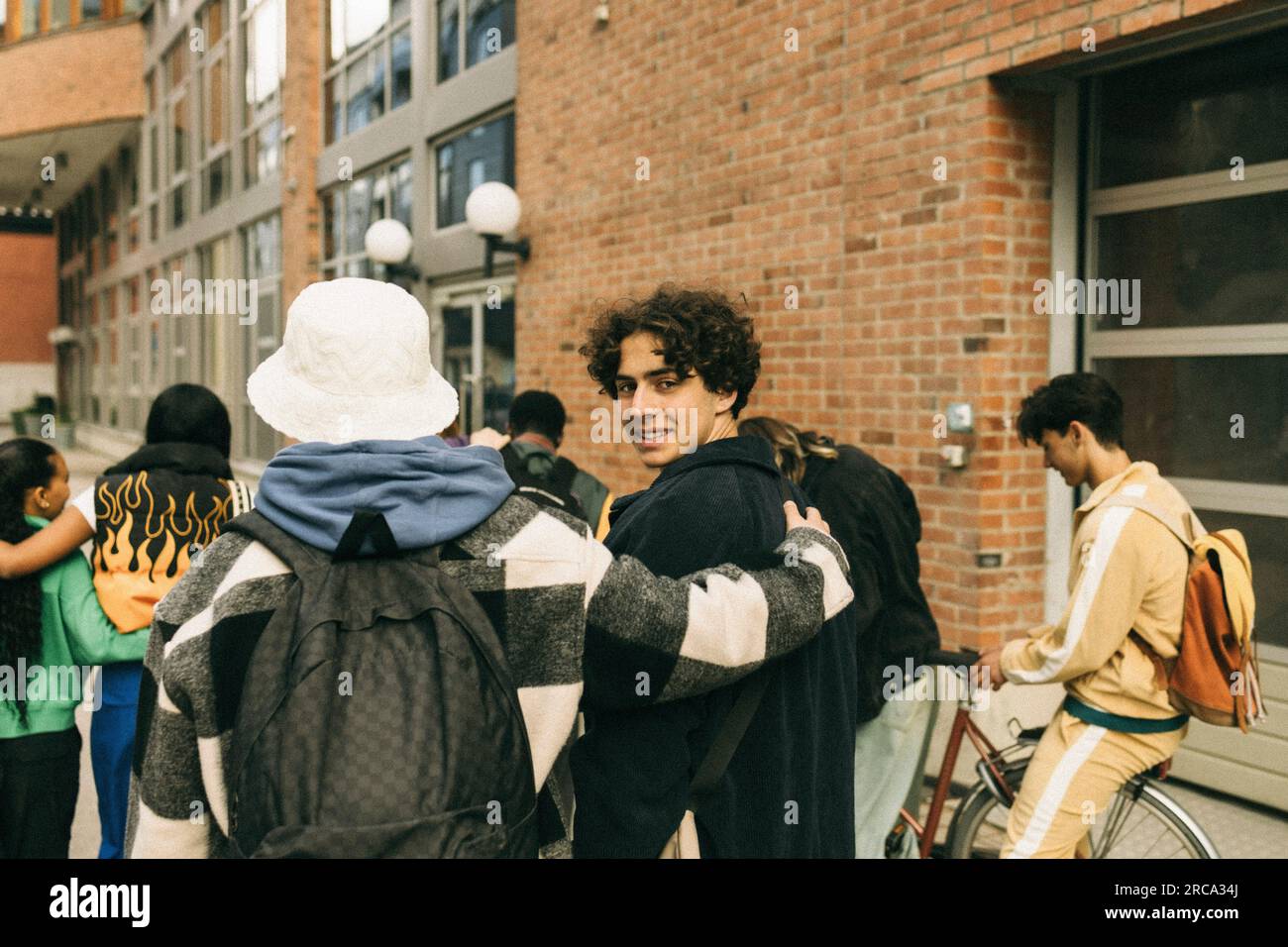 Lächelnder Teenager, der über die Schulter blickt, während er mit Freunden auf dem Bürgersteig spaziert Stockfoto