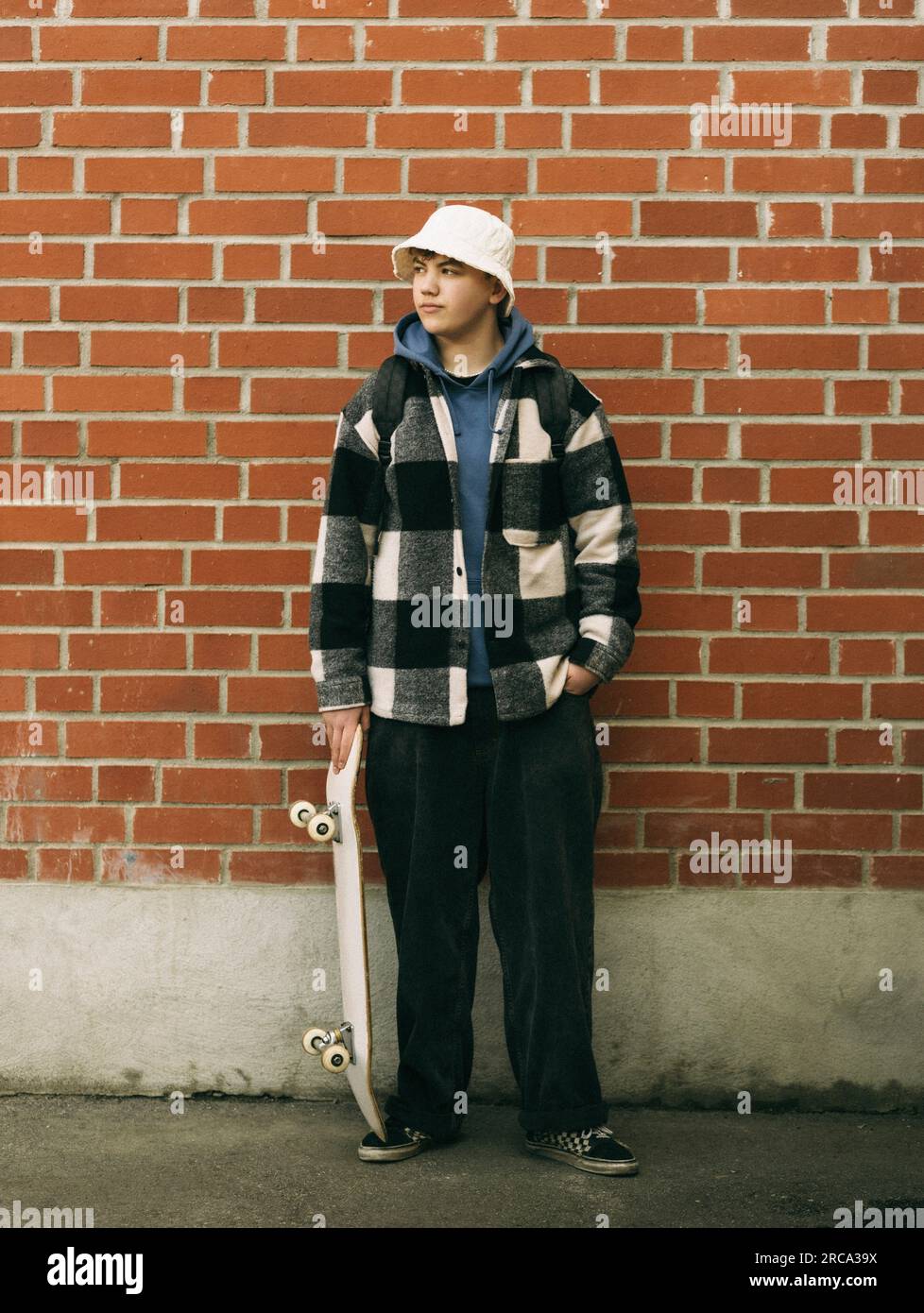 Junger Mann mit Skateboard, der vor einer Ziegelwand posiert Stockfoto