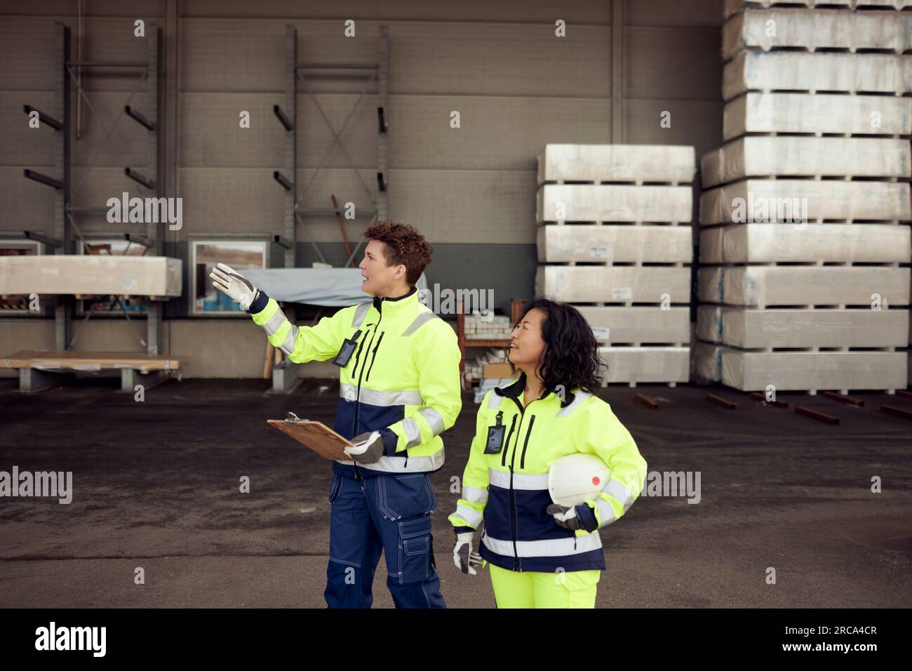 Arbeiterinnen in Arbeitsschutzkleidung, die im Lager diskutieren Stockfoto