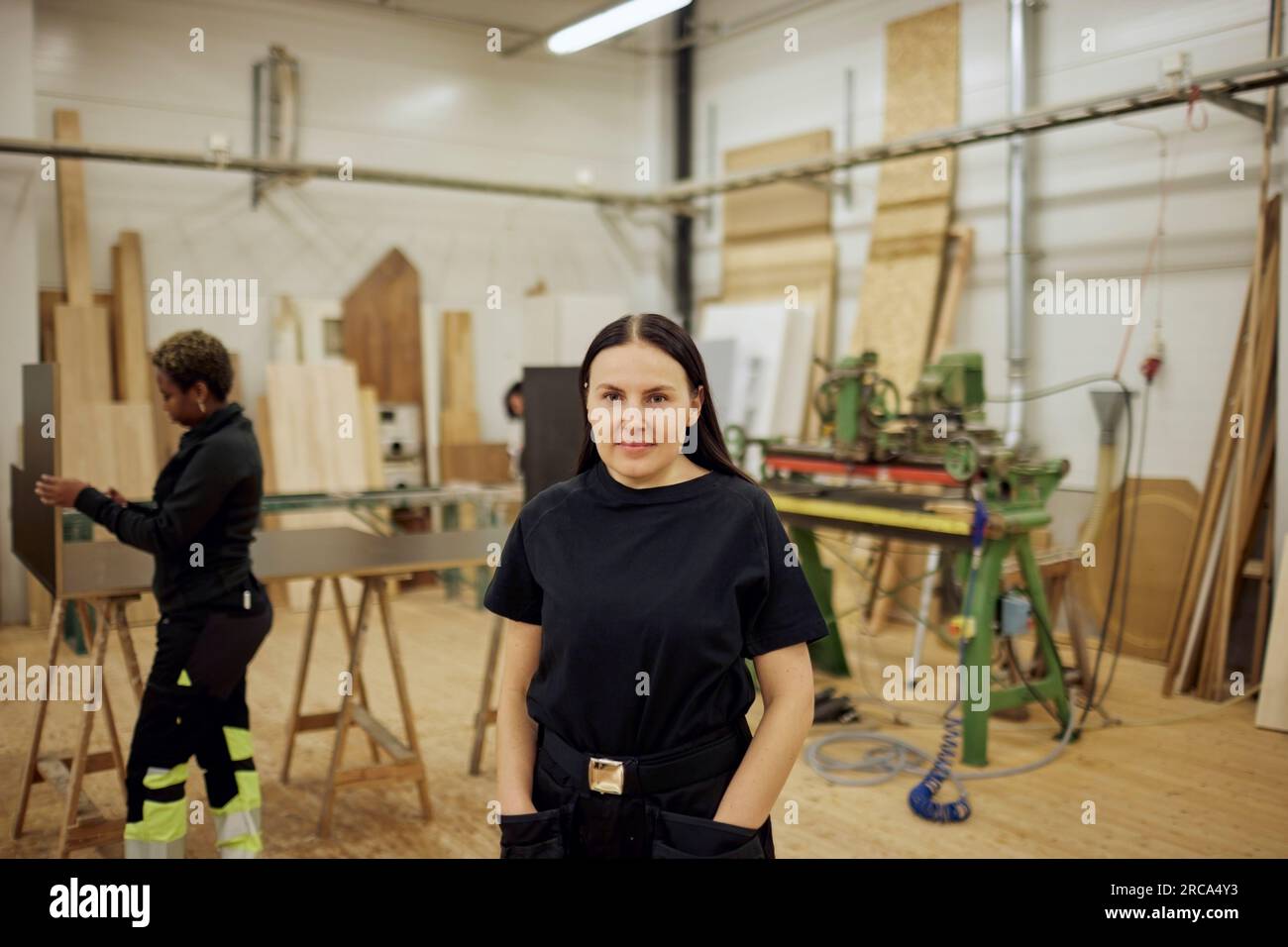 Porträt einer Zimmerlerin, die in der Werkstatt mit den Händen in den Taschen steht Stockfoto