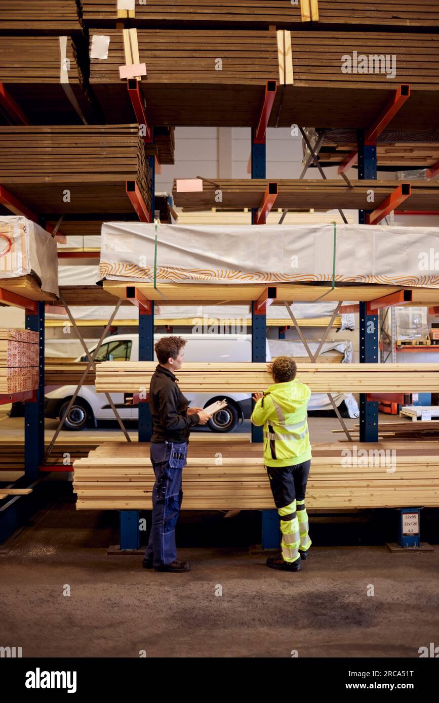 Multirassische weibliche Kollegen mit Brettern auf einem Regal diskutieren während der Arbeit in der Holzindustrie Stockfoto