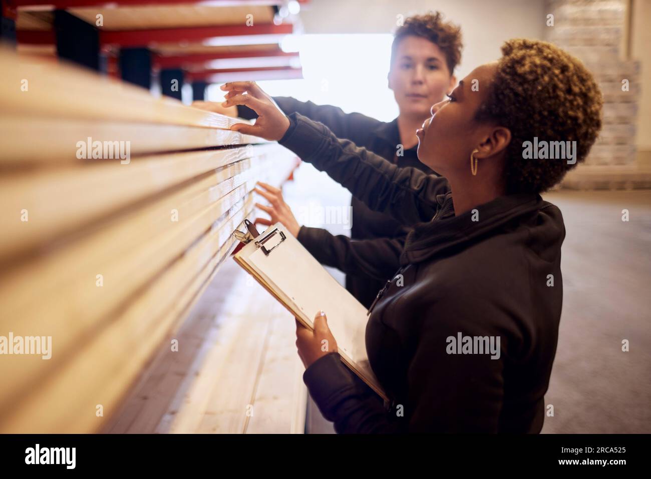 Multirassische weibliche Kollegen, die Bretter auf Regalen in der Holzindustrie untersuchen Stockfoto