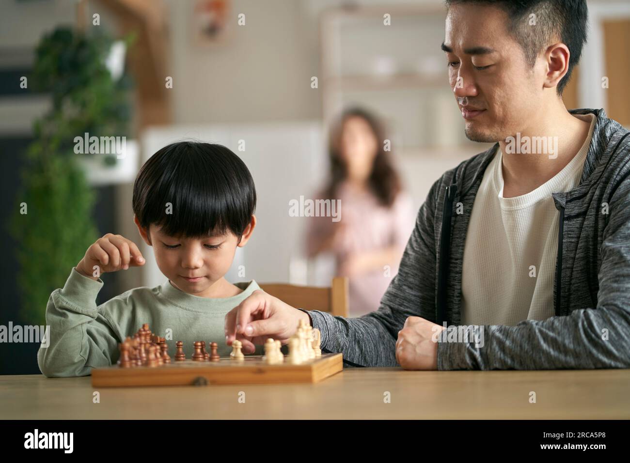 asiatischer Vater und Sohn sitzen zu Hause am Küchentisch und spielen Schach Stockfoto