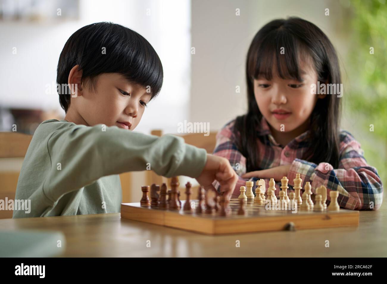 Zwei asiatische Kinder, Bruder und Schwester, die zu Hause am Tisch sitzen und Schach spielen Stockfoto