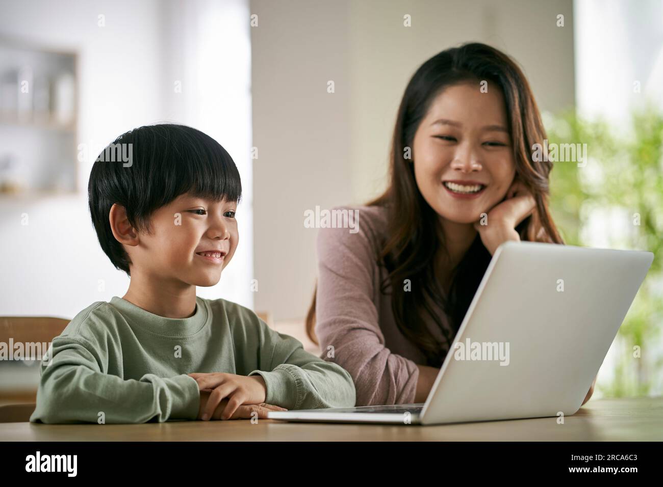 Glückliche asiatische Mutter und Sohn, die zu Hause an einem Tisch sitzen und sich einen Film mit einem Laptop anschauen Stockfoto