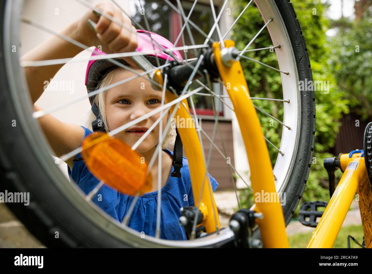 Ein kleines Mädchen repariert ein Rad mit einem Schraubenschlüssel im Hinterhof Stockfoto