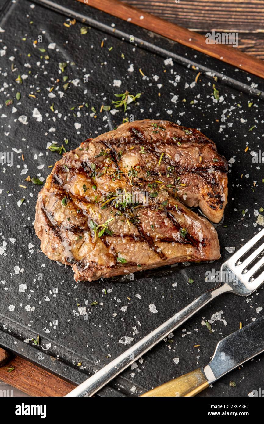 Gegrilltes Ribeye Steak mit Rosmarin und Thymian auf einem Steinschneidebrett Stockfoto