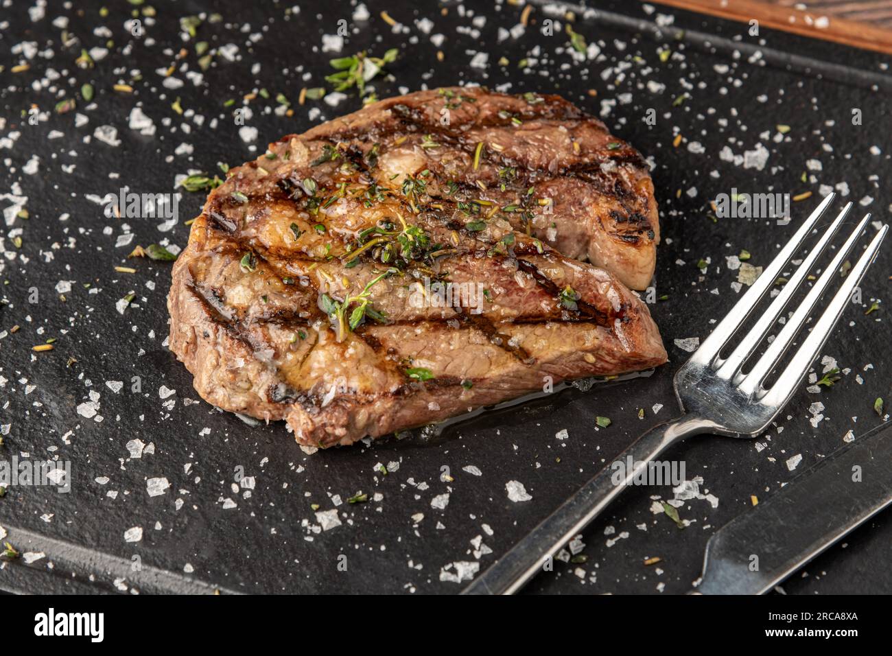 Gegrilltes Ribeye Steak mit Rosmarin und Thymian auf einem Steinschneidebrett Stockfoto