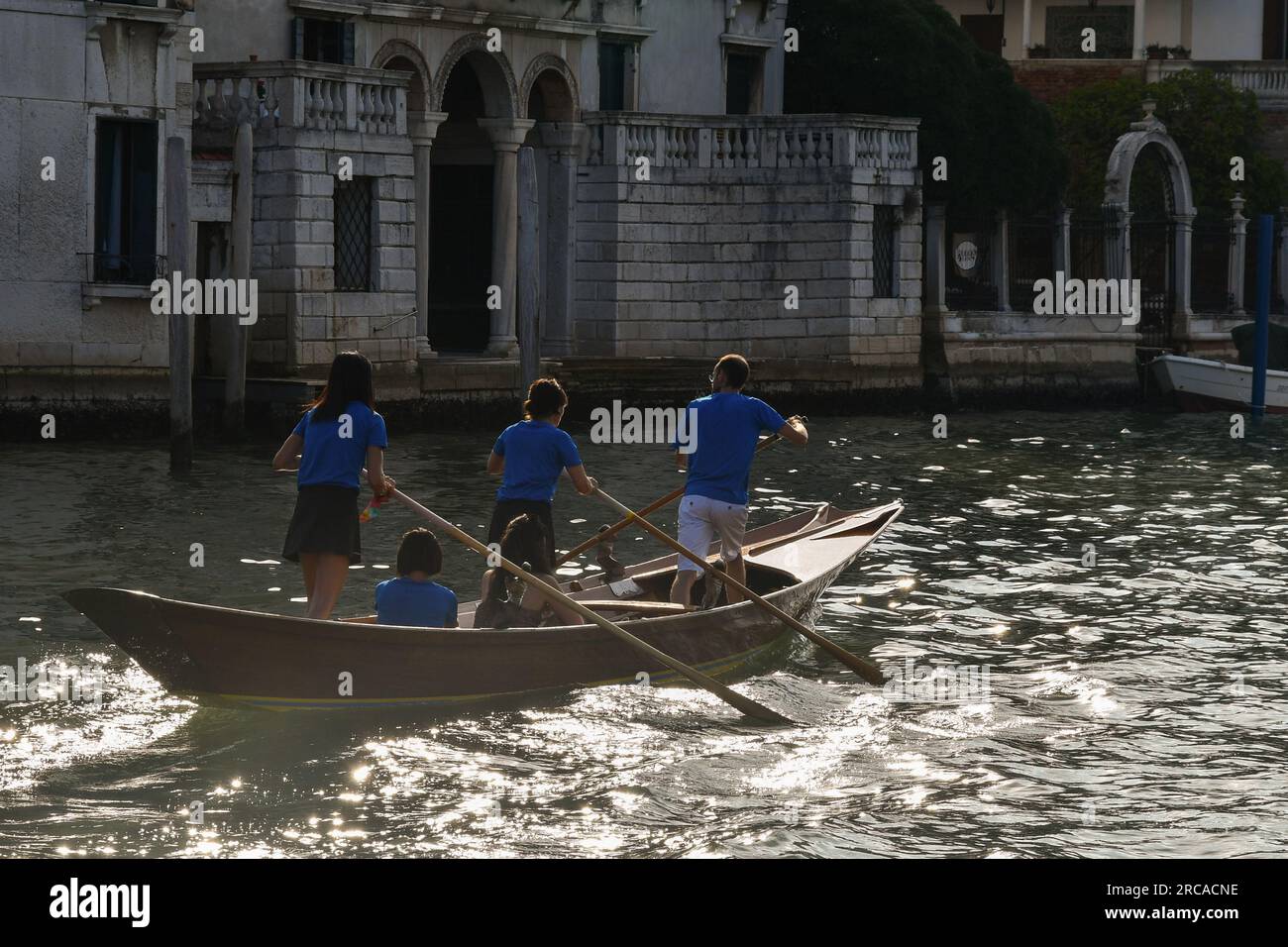 Eine Gruppe von Personen, die im venezianischen Reihenstil am Canale Grande bei Sonnenuntergang rudern, Sestiere von Dorsoduro, Venedig, Venetien, Italien Stockfoto