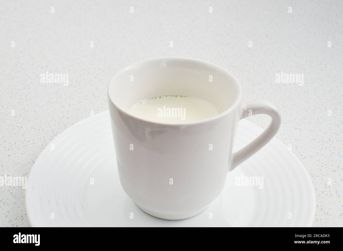 Genießen Sie einfachen Genuss: Eine weiße Tasse frische, leckere Milch auf einem hellen, einladenden Tisch. Stockfoto