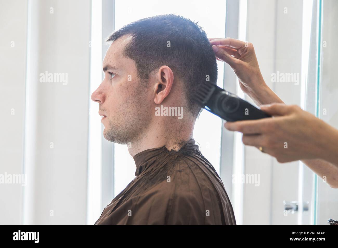 Eine Frau, die einem weißen Mann einen Haarschnitt in einem Heim verpasst. Familienleben und sorgenfreier moderner Lebensstil. Konzept von Komplizenschaft und Vertrauen. Schließen Stockfoto