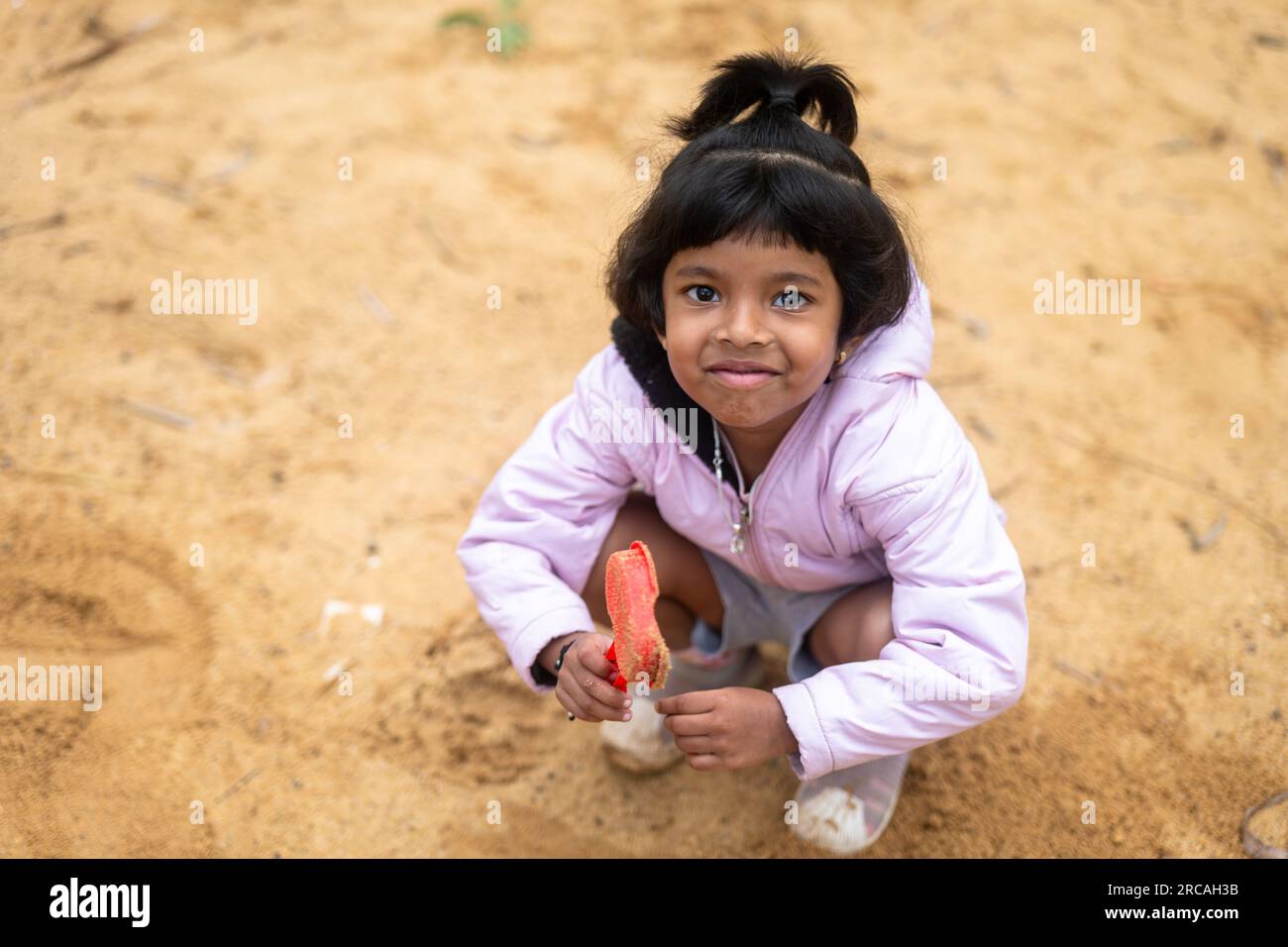 Ein kleines Mädchen hat viel Spaß beim Spielen im Schlamm. Sie lacht und lächelt, und sie sieht aus, als hätte sie die beste Zeit ihres Lebens. Stockfoto