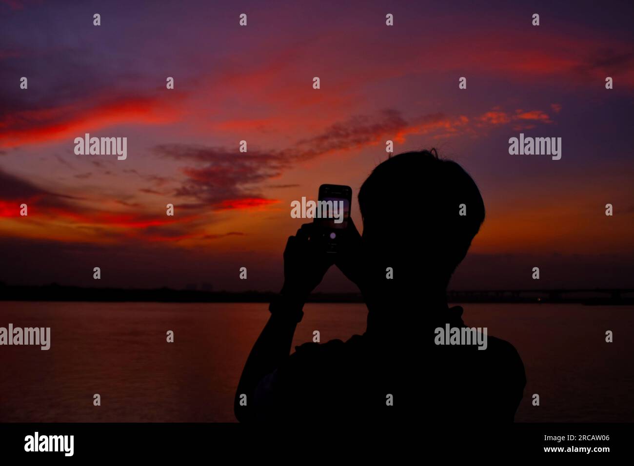 Ein Mann, der den Sonnenaufgang unten am Fluss beobachtet Stockfoto