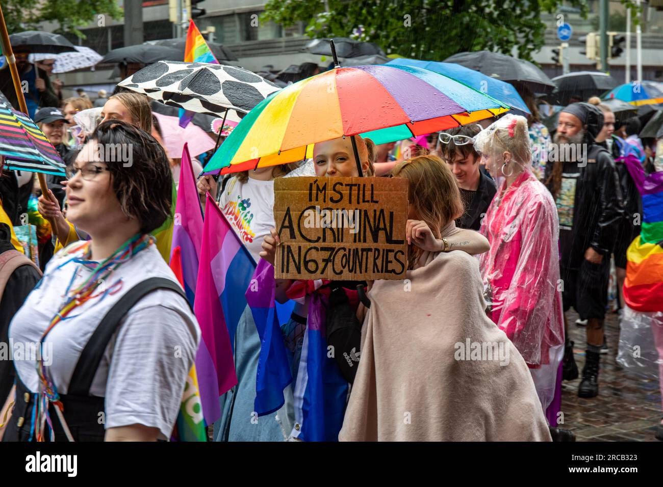 Junge Frau mit Regenbogenschirm und einem Pappschild auf der Helsinki Pride 2023 Parade in Helsinki, Finnland Stockfoto