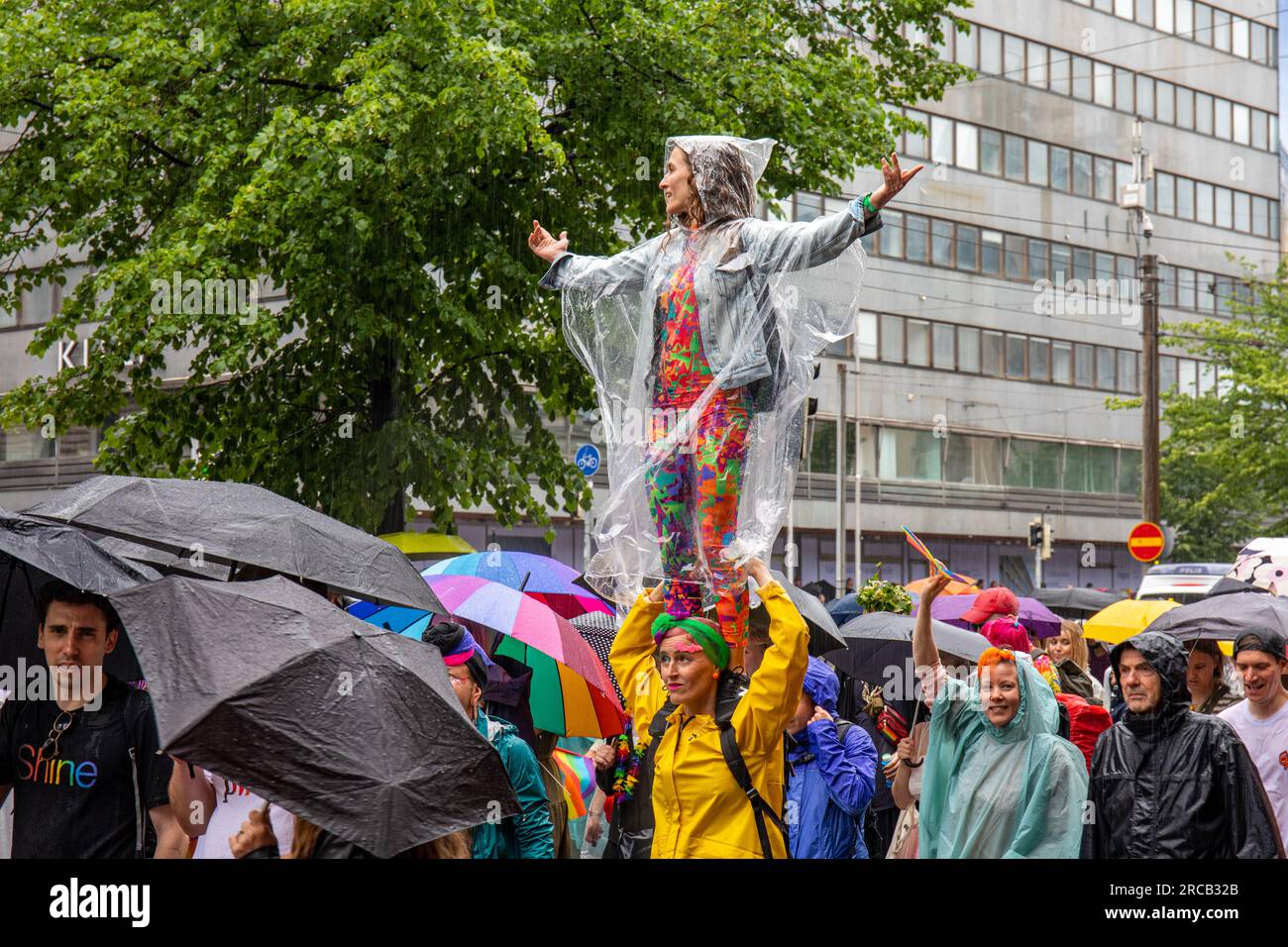 Frau mit Einweg-Regenjacke auf den Schultern eines Freundes bei der Helsinki Pride 2023 Parade in Helsinki, Finnland Stockfoto