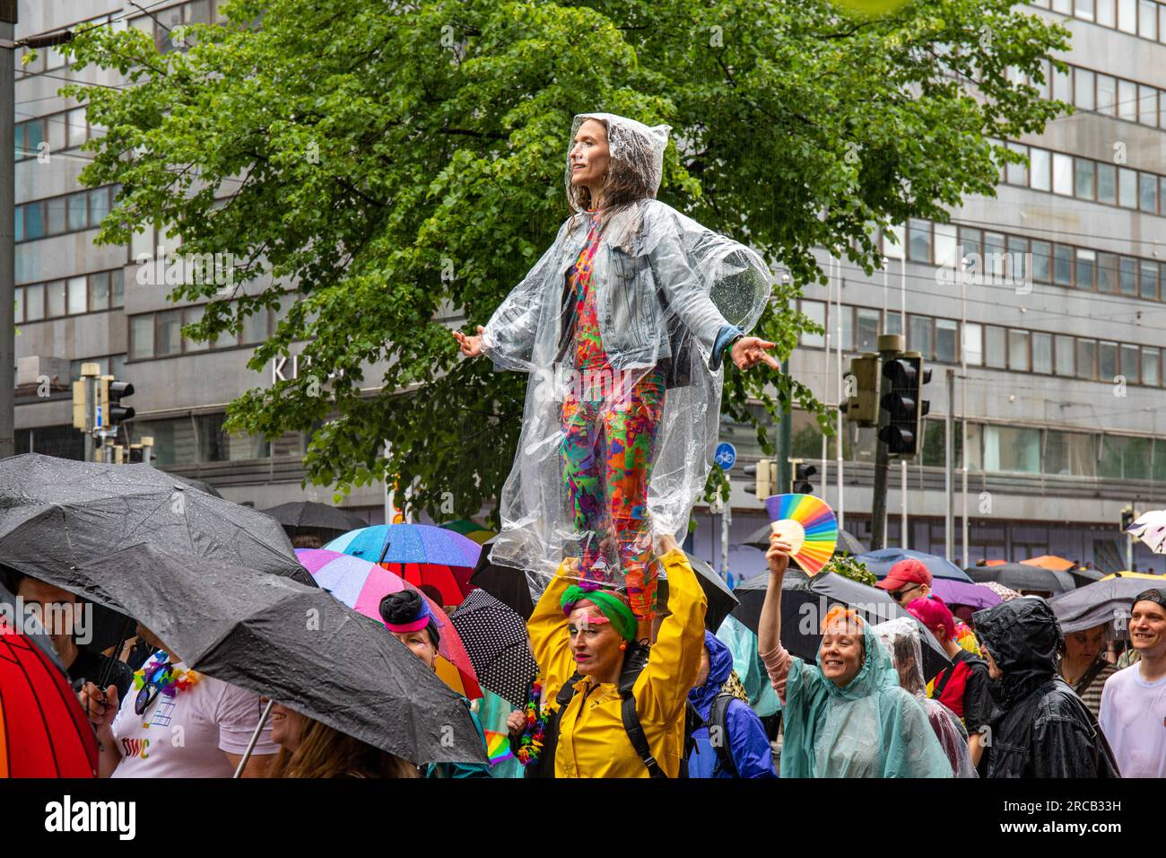 Frau mit Einweg-Regenmantel, die an einem Regentag auf den Schultern eines Freundes bei der Helsinki Pride 2023 Parade in Helsinki, Finnland, steht Stockfoto