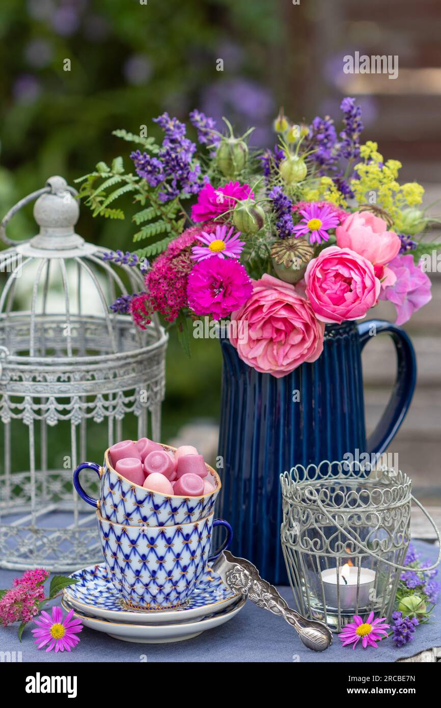 Tischanordnung mit Süßigkeiten in Porzellanbecher, Blumenstrauß und Tischlaterne Stockfoto