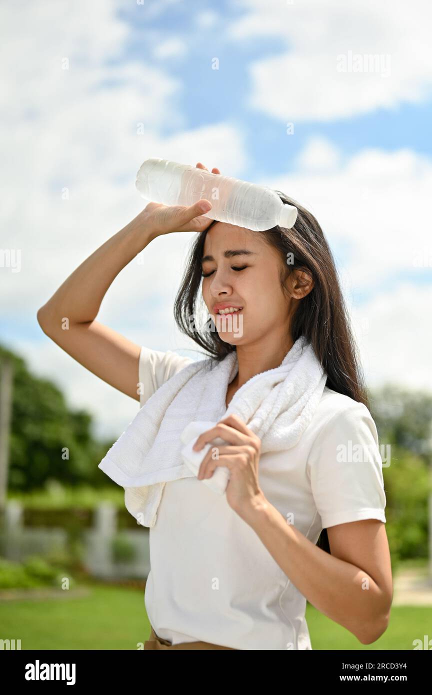 Das Porträt einer schwitzenden Asiatin in Sportbekleidung, die sich heiß und müde fühlt, ruht nach einem langen Lauf im Park an einem sonnigen Tag. Sommer-Aktivitätskonzept Stockfoto