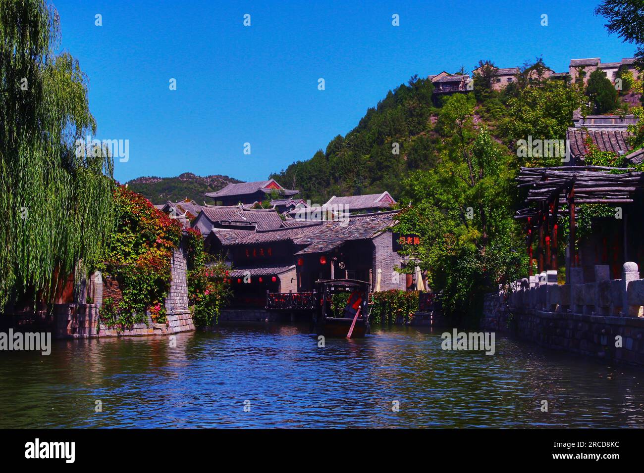 Entdecken Sie die harmonische Mischung aus einem wunderschönen Fluss, grünen Bäumen und traditionellen Häusern, die sich in der sanften Umarmung des Sonnenlichts im Freien sonnen. Stockfoto
