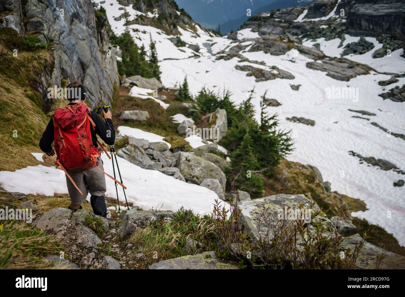 Männlicher Wanderer steigt den Berg hinab, mit Stöcken in rotem Rucksack, Kanada Stockfoto