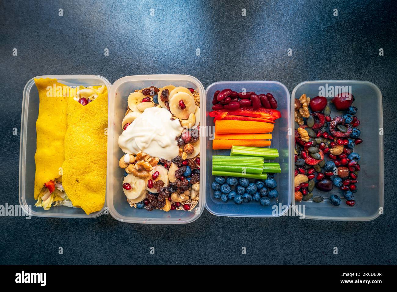 Schachteln mit gesundem Essen voller bunter Gemüse und Obst. Nüsse, Heidelbeeren, Joghurt, Granatäpfel, Bananen, Glutenfreie Pfannkuchen, Rosinen, celer Stockfoto