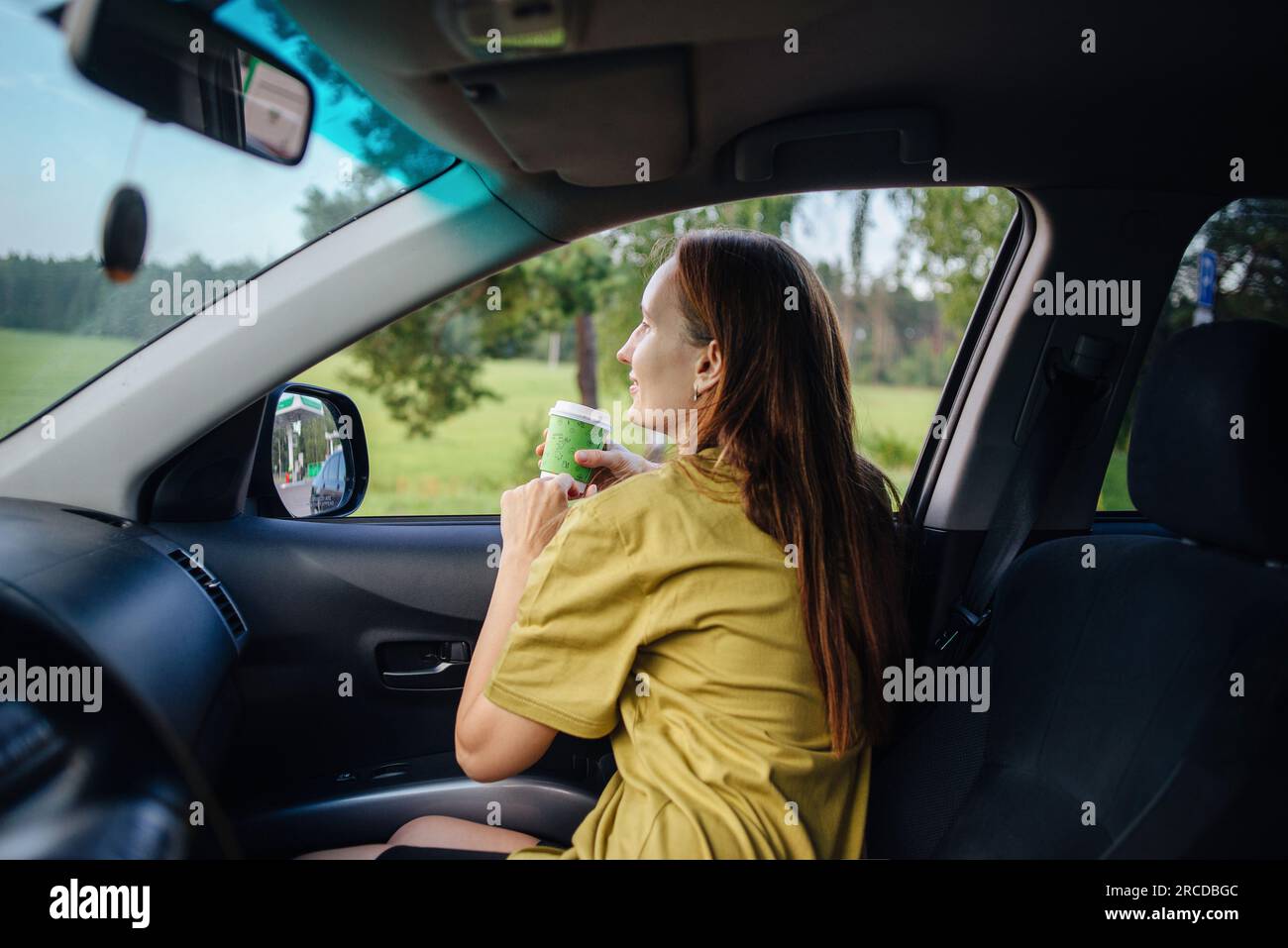Ein Mädchen auf einer Reise sitzt in ihrem Auto und trinkt Kaffee Stockfoto