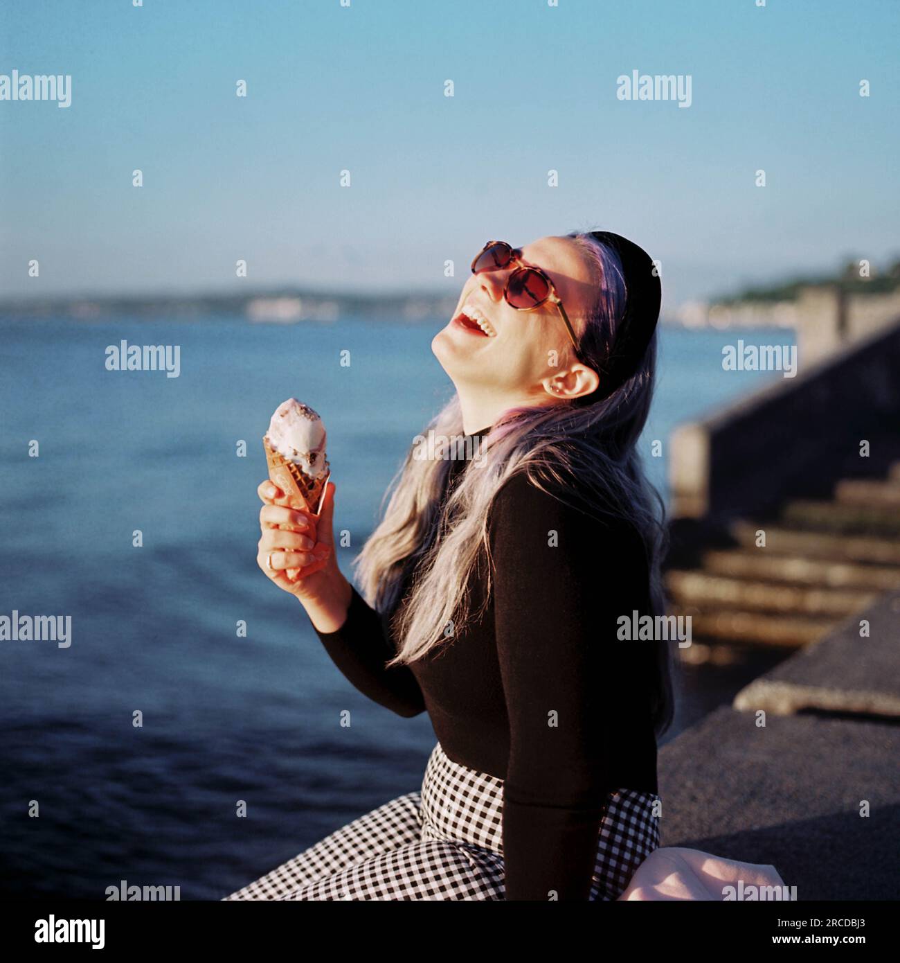 Eine Frau mit lila Haaren isst Eis auf einem Dock am Alki Beach Stockfoto