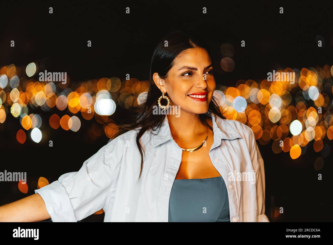 Wunderschöne Frau auf einem Balkon mit verwischten Lichtern im Hintergrund Stockfoto