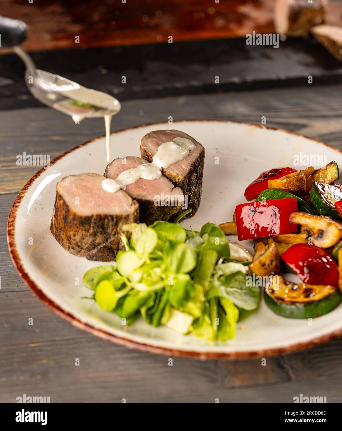 Der Koch gießt den Salat aus einem Löffel mit Soße. Stockfoto