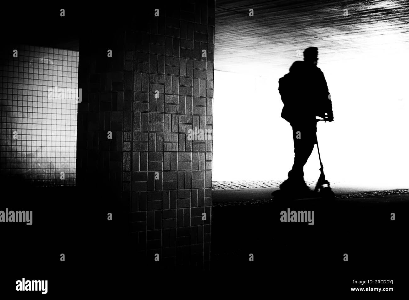 Künstlerisch grobkörniges Bild einer Silhouette eines Mannes, der einen Kickroller in unscharfer Bewegung fährt. Stockfoto