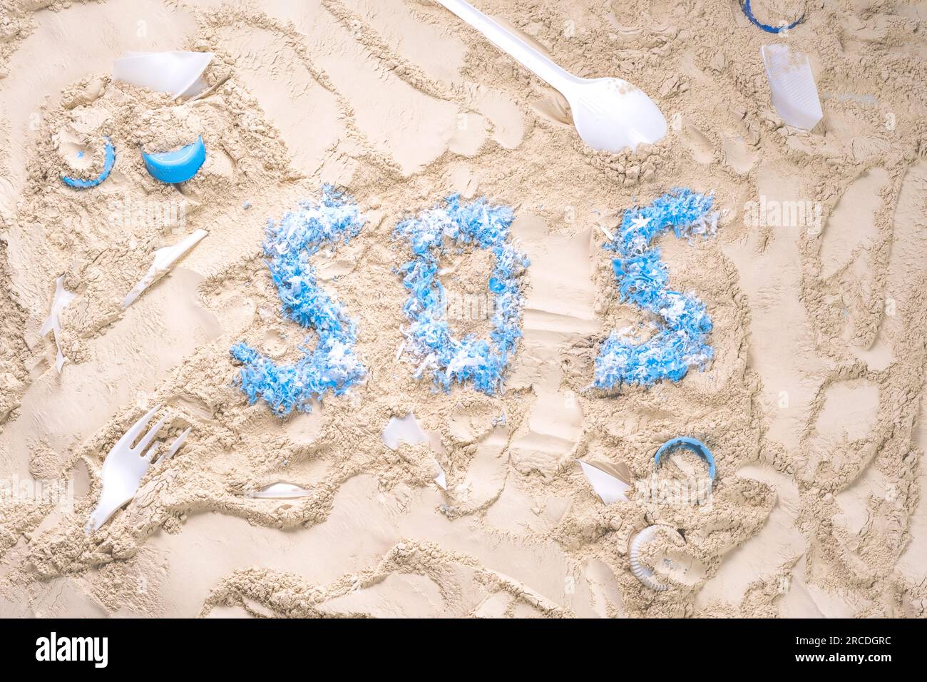 SOS-Wort mit blauen Plastikstücken auf dem Sand. Hilfe! Hilfe! Rette den Ozean. Der Begriff der Verschmutzung und die Abhängigkeit von Kunststoff. Stockfoto