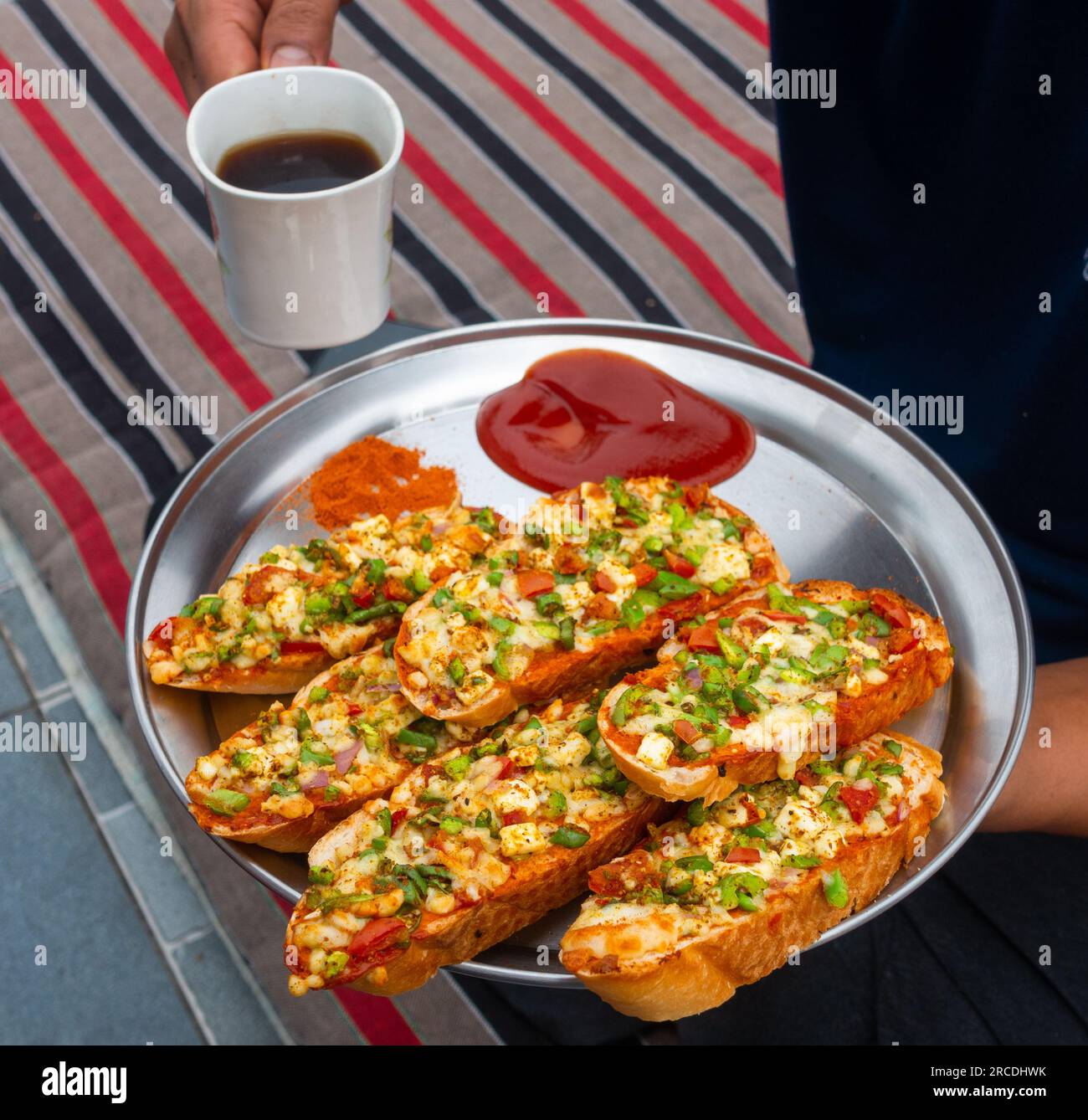 Hände mit schwarzem Kaffee und hausgemachtem Ingwer-Knoblauchbrot mit Käse und indischen Kräutern. Indien Stockfoto